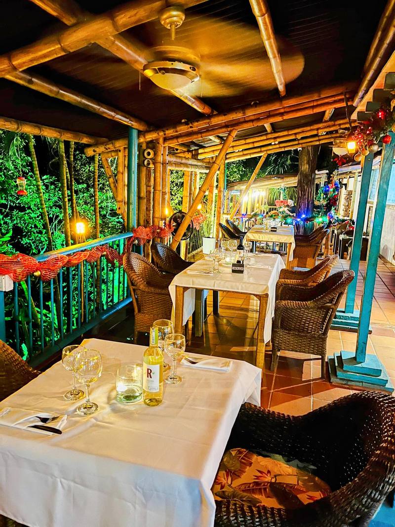 Terraza del restaurante con ventiladores de techo, mesas servidas y vegetación tropical