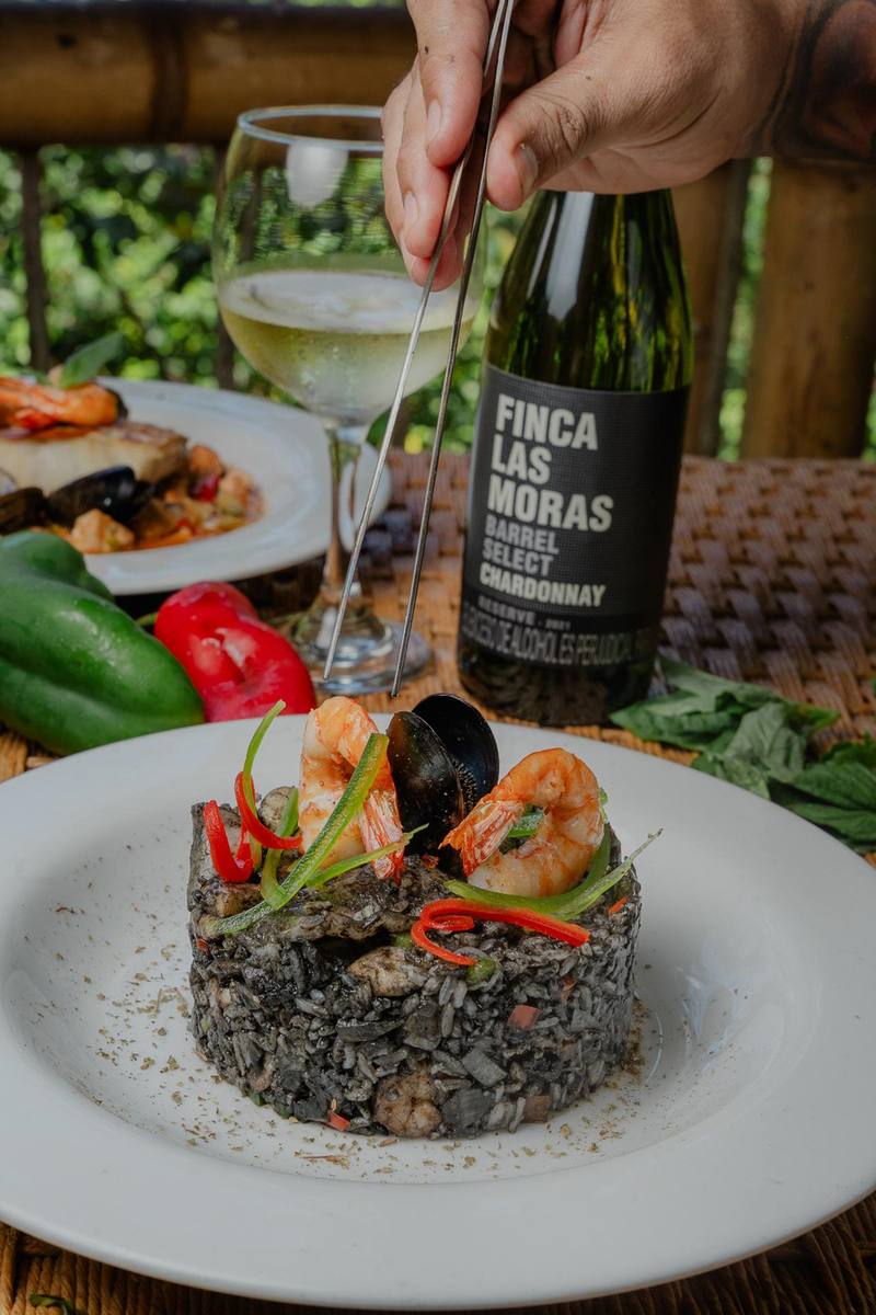 Sirviendo vino blanco junto a un plato de arroz negro con mariscos
