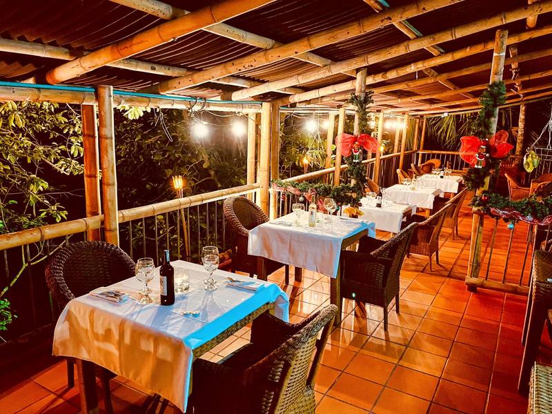 Terraza al aire libre con techo de bambú, luces cálidas y mesas servidas entre la selva